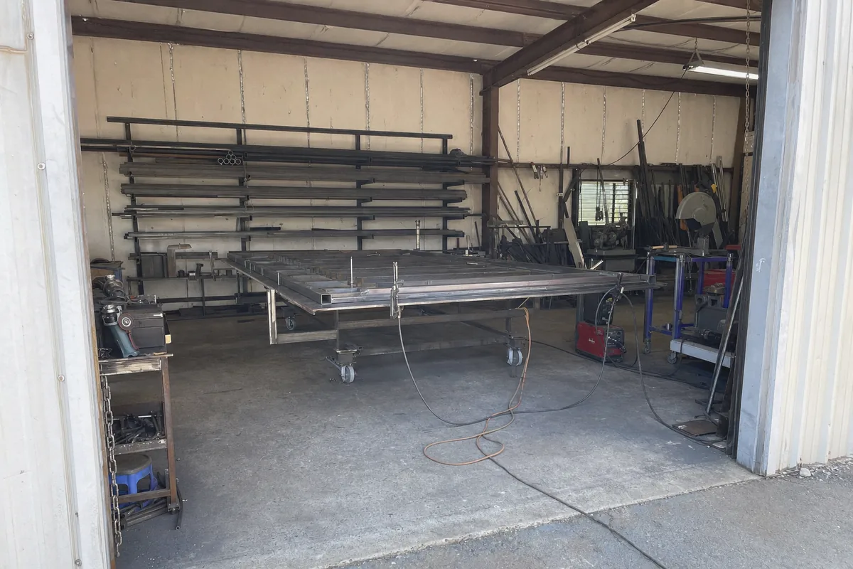 Interior of the gate fabrication workshop with a gate frame clamped flat on the layout table